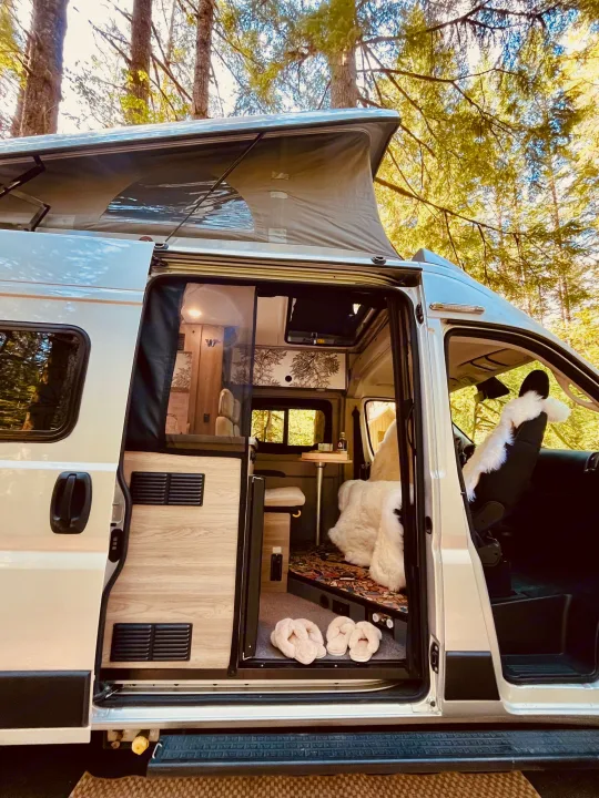 Spacious rv rental camper van with open door, showing cozy interior, pop-top roof, and comfy slippers. Ideal for a nature retreat.. Winnebago Eurovan Camper Eurovan Camper 2023