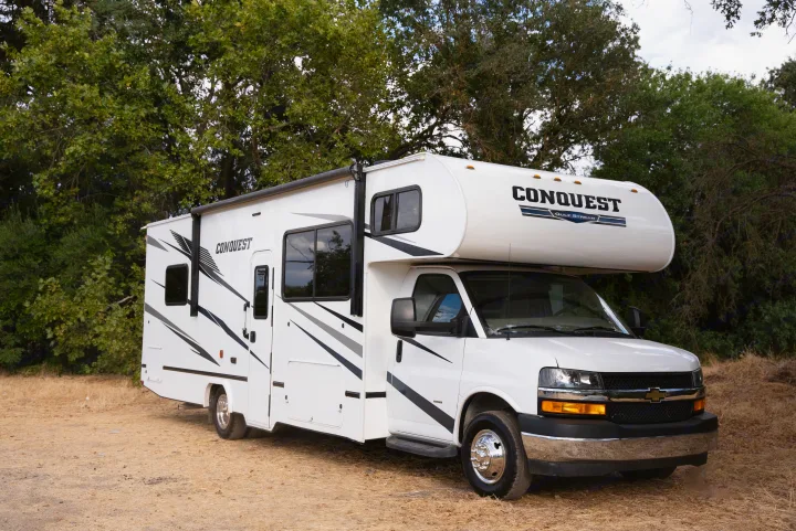 White Class C RV rental (Conquest Gulf Stream) parked on dirt, ready for travel. Trees frame this adventure motorhome.. Gulf Stream Conquest 2022