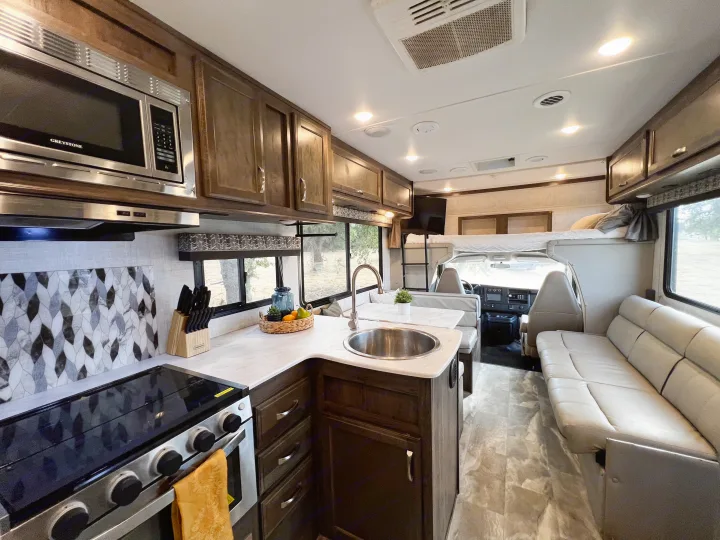 An RV rental's interior shows a kitchen with microwave, stove, sink, dining area, sofa, and overhead bunk.. Gulf Stream Conquest 2022