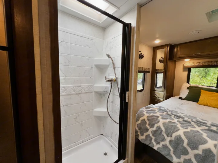 RV rental interior: a bright, tiled shower with skylight and a cozy bedroom with a patterned blanket.. Gulf Stream Conquest 2022