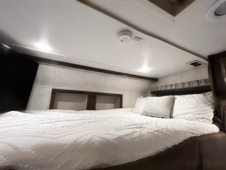Modern RV rental bedroom with crisp white bedding, wall-mounted TV, and ample overhead storage.. Gulf Stream Conquest 2022