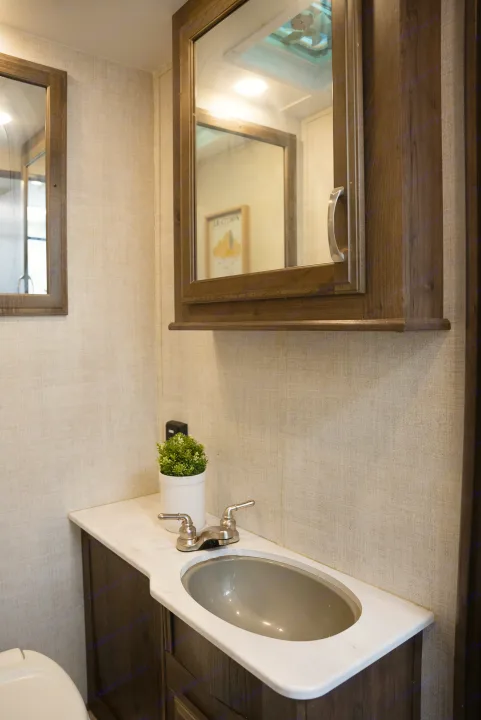 Inside an RV rental: a compact bathroom with textured walls, white counter, modern sink, and mirrored cabinets.. Gulf Stream Conquest 2022
