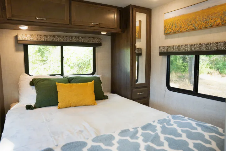 Spacious RV rental bedroom with a cozy bed, vibrant pillows, windows with outdoor views, and built-in storage.. Gulf Stream Conquest 2022