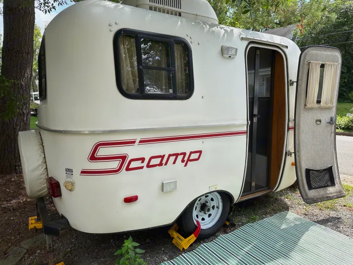 White Scamp RV rental parked outdoors, showing its side, window, and open door. Perfect for compact camping.. Scamp Scamp Trailer 2011