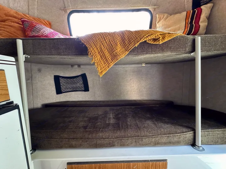 An RV rental's cozy interior features stacked bunk beds, a window, and soft cushions, perfect for camping trips.. Scamp Scamp Trailer 2011