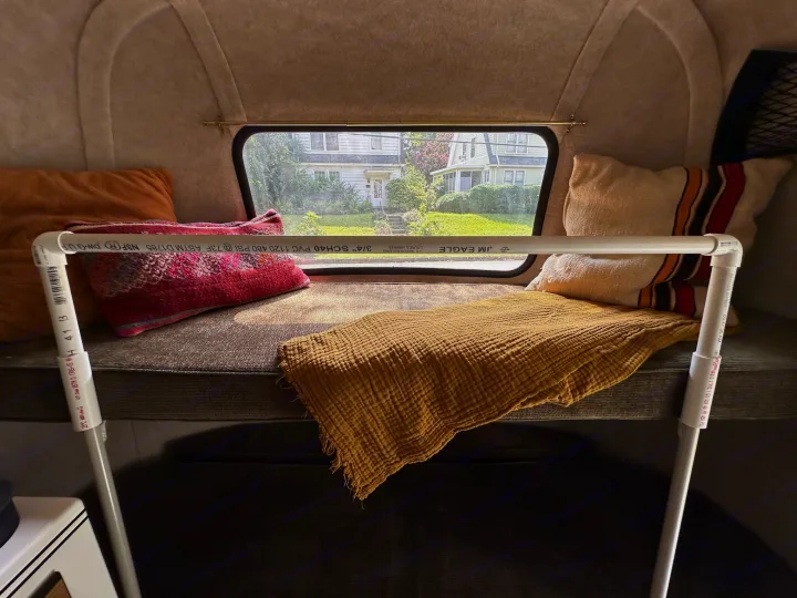 Cozy RV rental interior with bed, pillows, and window view of houses. A white PVC pipe structure is visible.. Scamp Scamp Trailer 2011