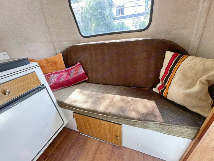 View inside an rv rental, featuring a brown bench, colorful cushions, window, and a small Dometic fridge.. Scamp Scamp Trailer 2011