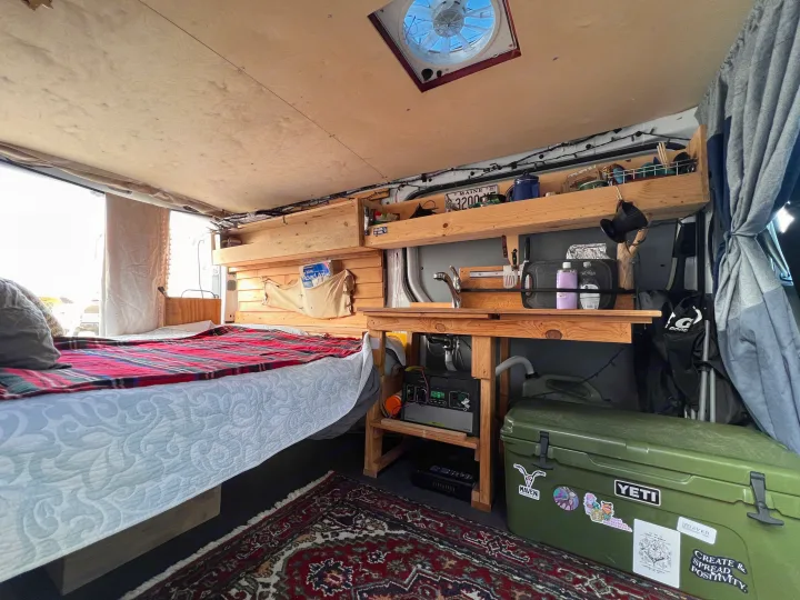 Cozy RV rental interior showing a comfortable bed, compact kitchen area, and clever wooden storage for van life.. Mercedes-Benz Sprinter 2012