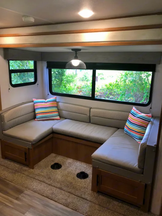Cozy RV rental interior featuring a U-shaped dinette with soft cushions, windows, and lush outdoor views for travel.. Forest River Prime Time Avenger 24BHS 2023