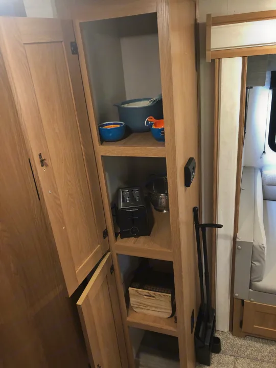 Organized RV rental cabinet showcasing kitchen items like a toaster & bowls, plus a dustpan & broom. Efficient space utilization.. Forest River Prime Time Avenger 24BHS 2023