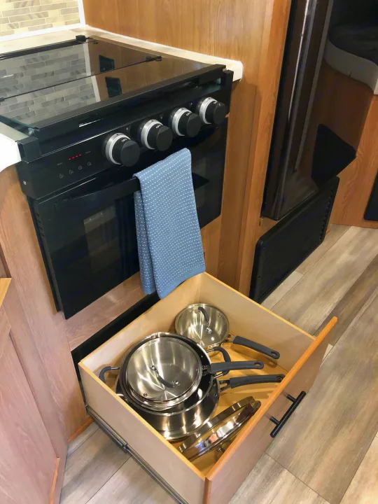 RV rental kitchen features a compact black stove/oven, glass cooktop, and a drawer of stainless steel pots.. Forest River Prime Time Avenger 24BHS 2023