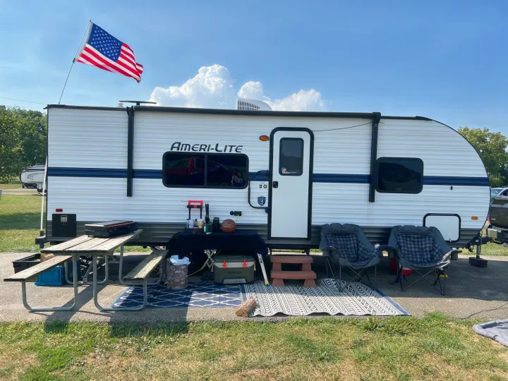 Spacious Ameri-Lite RV rental at a sunny campsite, adorned with an American flag, picnic table, and outdoor seating.. Gulf Stream Ameri-Lite 2022