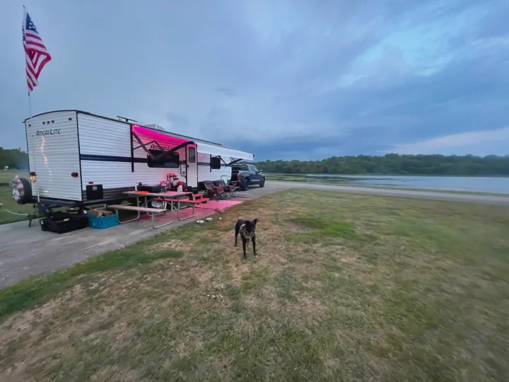 RV rental parked by a lake at dusk, with a dog on the grass. An inviting campsite for serene outdoor travel.. Gulf Stream Ameri-Lite 2022