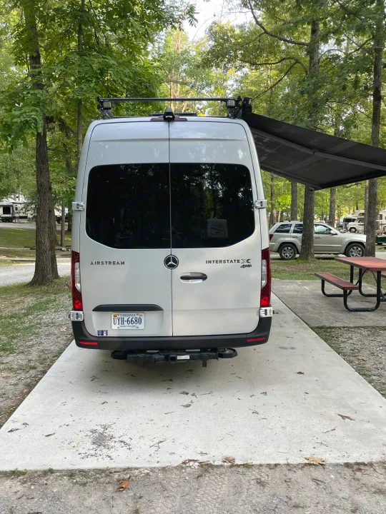 Rear view of an Airstream Interstate X 4WD RV rental parked at a serene campground site under an awning.. Airstream Interstate 2023