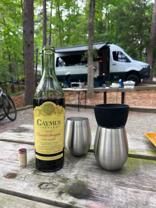 Relaxing at an RV rental site with Caymus Cabernet Sauvignon wine & insulated tumblers on a picnic table.. Airstream Interstate 2023