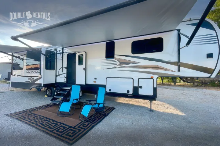 Spacious Durango Gold RV rental, featuring an extended awning with LED lights, and a cozy outdoor setup with blue chairs.. KZ Durango Gold 2022