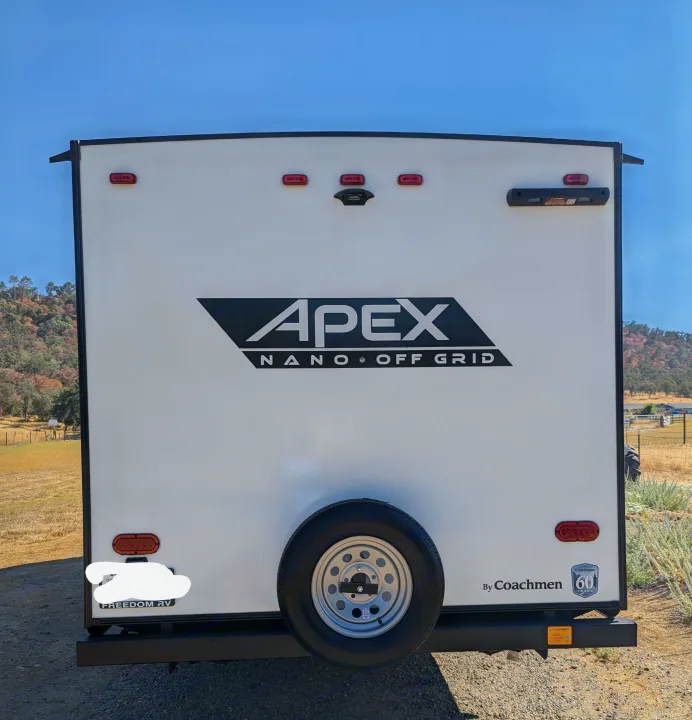 The rear of an APEX NANO OFF GRID travel trailer with a spare tire, perfect for an RV rental or off-grid adventures.. Coachmen Apex Nano 2024