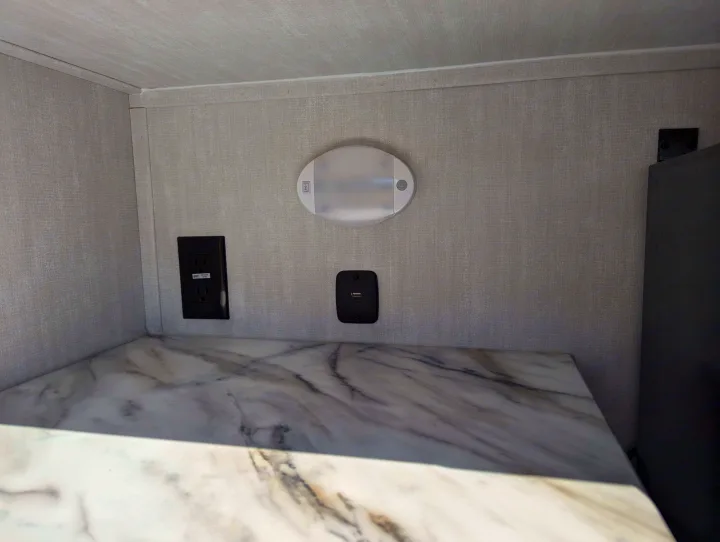 Modern RV rental interior with power outlets, USB ports, and LED light above a marble-look countertop, offering convenience.. Coachmen Apex Nano 2024