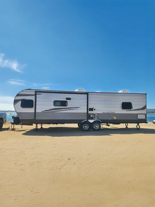 RV rental trailer on a sandy beach. Enjoy beachfront camping and travel under a bright blue sky by the ocean.. Forest River Aurora Aurora 2024