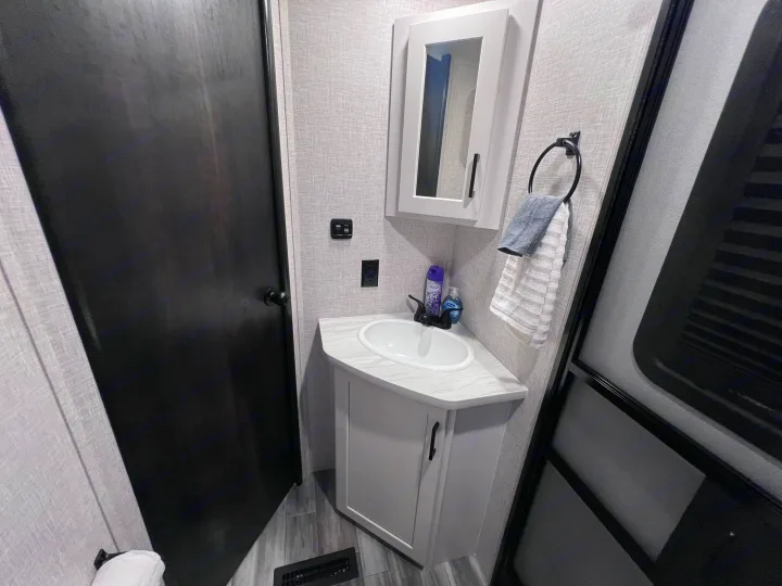 RV rental bathroom features a compact corner sink, mirrored cabinet, and handy towel ring.. Jayco Jay Feather 2024