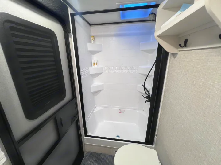 Bright, clean RV rental bathroom with a modern white shower, built-in shelves, skylight, and a toilet to the right.. Jayco Jay Feather 2024