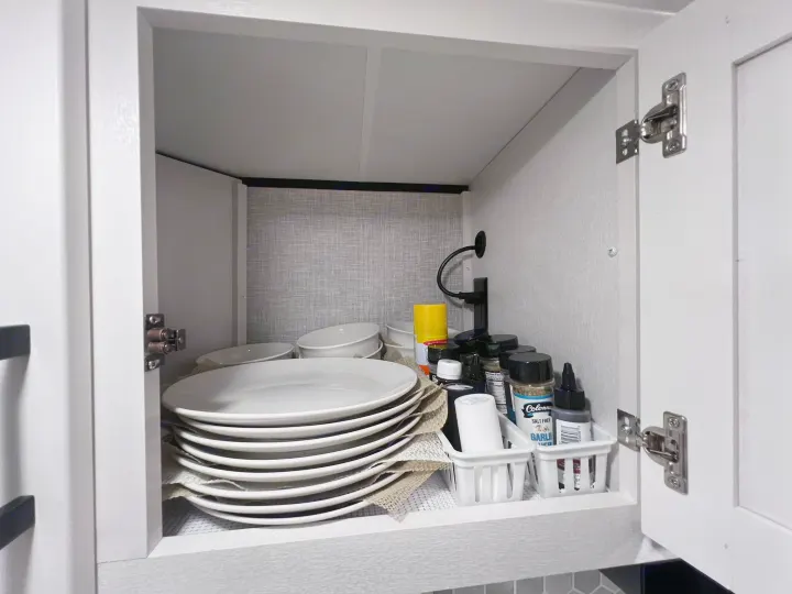 Well-organized RV rental kitchen cabinet: stacked white plates, bowls, spices, and cooking essentials neatly stored.. Jayco Jay Feather 2024