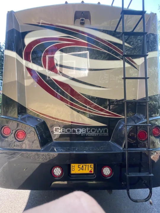 Full rear view of a tan and black Georgetown Forest River RV, featuring a ladder, lights, and backup camera. Great for an rv rental adventure!. Georgetown GT5 2019
