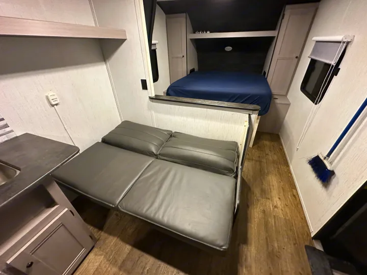 This RV rental interior features a cozy bed, convertible seating, and a compact kitchen area with light walls and wood-look flooring.. Heartland RVs Trail Runner 2022