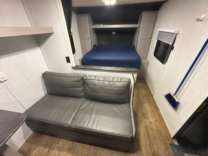 Inside this RV rental: a cozy gray sofa, elevated bed, and compact living space with wood-look flooring.. Heartland RVs Trail Runner 2022