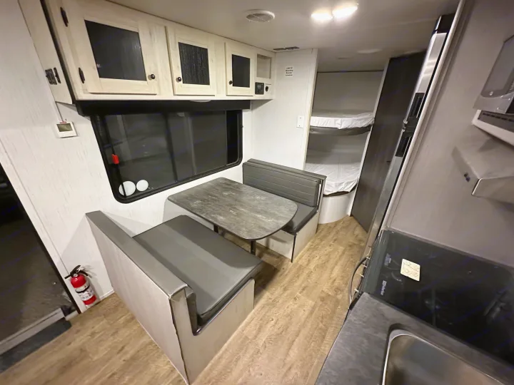 Modern RV rental interior: Dinette, overhead cabinets, kitchen, bunk beds, and wood-look flooring.. Heartland RVs Trail Runner 2022