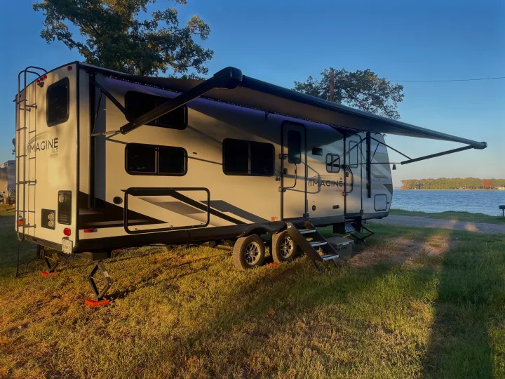 Relaxing lakeside with a white Grand Design Imagine travel trailer, perfect for an RV rental getaway.. Grand Design Imagine XLS 2024