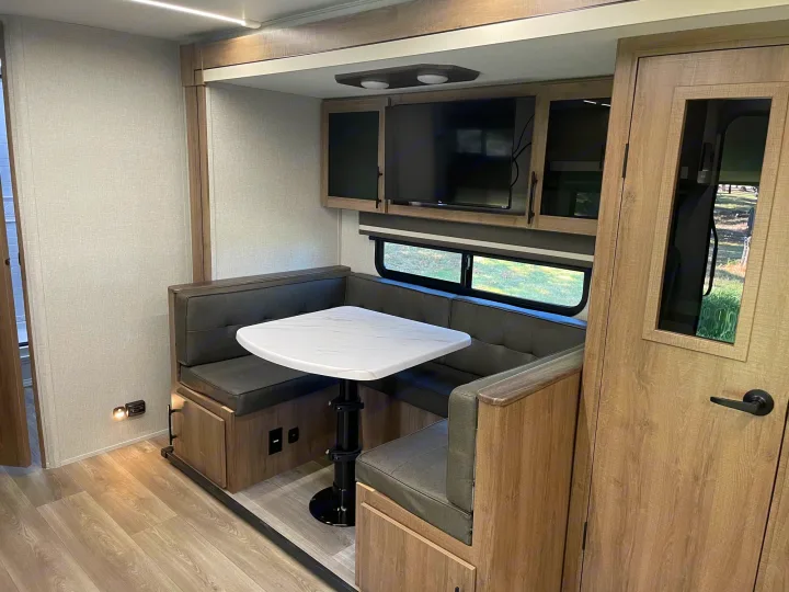 Modern RV rental interior featuring a spacious U-shaped dinette with table, TV, and overhead cabinets.. Grand Design Imagine XLS 2024