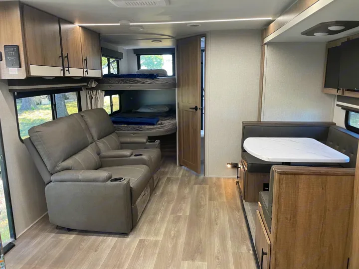 Modern RV rental interior: grey recliners, bunk beds, and a dinette with light wood floors.. Grand Design Imagine XLS 2024