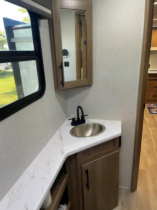 RV rental bathroom vanity: corner sink, black faucet, mirror cabinet, & large window. Clean and modern interior.. Grand Design Imagine XLS 2024
