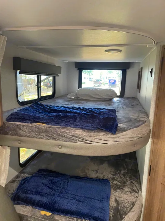 Two cozy bunk beds in an RV rental, each with a grey sheet and blue blanket, offering a comfortable sleeping area.. Grand Design Imagine XLS 2024