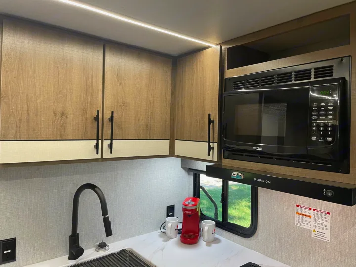 RV rental kitchen featuring modern wood cabinets, microwave, sink, and coffee maker for a comfortable stay.. Grand Design Imagine XLS 2024