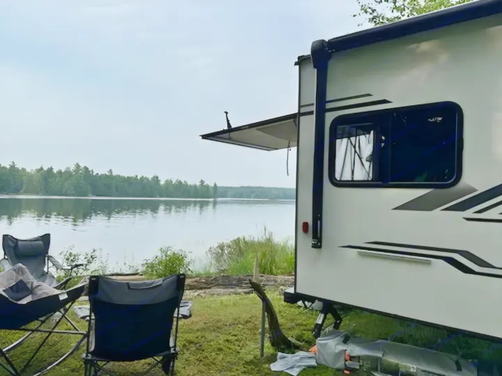 Lakeside RV rental setup with an extended awning and two chairs, inviting a peaceful outdoor escape.. KZ Escape Hatch 2022