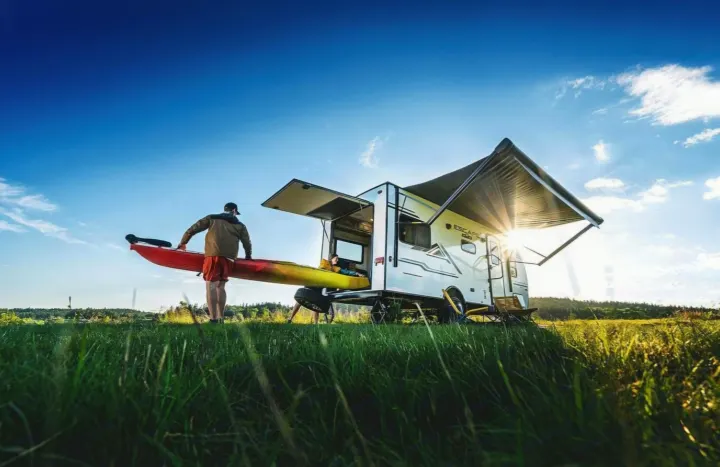 Perfect rv rental setup for outdoor adventures! Kayaker approaches camper in sunny field with blue sky.. KZ Escape Hatch 2022