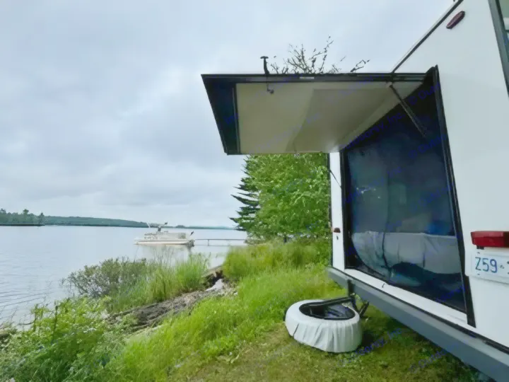 Enjoy the waterfront view from this RV rental, parked lakeside with a pontoon boat docked under a cloudy sky.. KZ Escape Hatch 2022