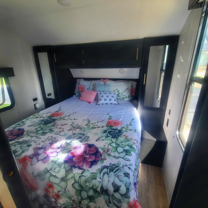 Bright RV rental bedroom showcasing a bed with floral/succulent bedding, overhead cabinets, and mirrored wardrobes.. Forest River Cherokee Grey Wolf 2022