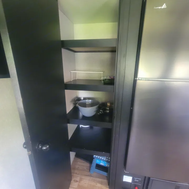 View inside an RV rental's open pantry with dark shelves holding kitchenware. A fridge is. Forest River Cherokee Grey Wolf 2022