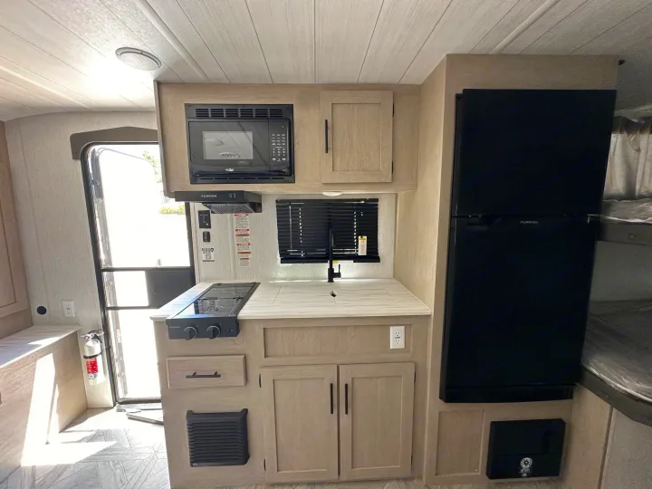 RV rental: Bright, modern RV interior showing kitchen area with microwave, stovetop, sink, fridge, and entry door.. Forest River Wildwood Platinum 2024