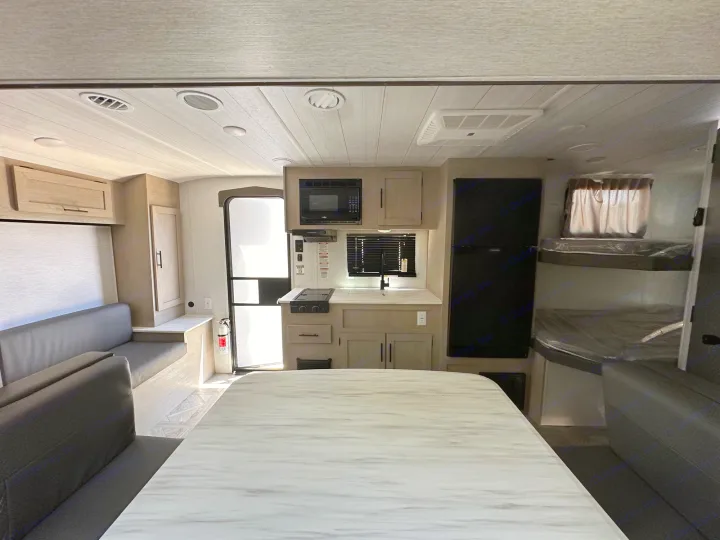 Wide shot of a modern RV rental interior: dinette seating, full kitchen, fridge, and bunk beds visible.. Forest River Wildwood Platinum 2024