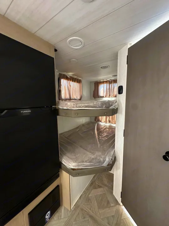 RV rental bunkhouse interior featuring new beds with plastic covers & a Furrion fridge. Ideal for family travel.. Forest River Wildwood Platinum 2024