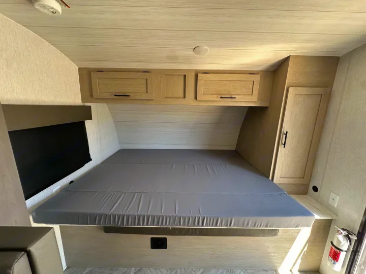 Cozy RV rental interior: a bedroom with a grey bed, overhead storage cabinets, and a visible fire extinguisher.. Forest River Wildwood Platinum 2024