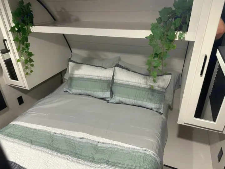 This inviting RV rental bedroom features a comfy bed with green accents, white overhead storage, and plant decor.. Jayco Jay Flight 2024