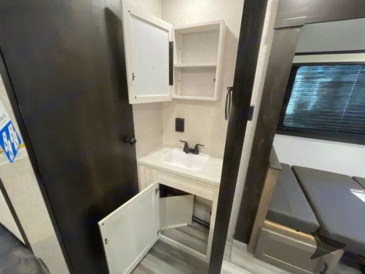 Compact RV rental interior: A small sink & open cabinets, plus a dinette under a window.. Jayco Jay Flight 2024