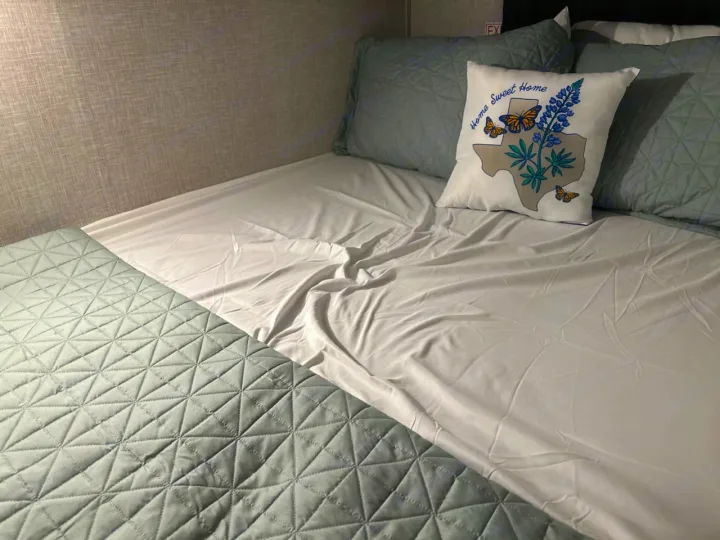 Cozy RV rental bed with soft green quilted bedding and a decorative Texas "Home Sweet Home" pillow for comfortable travel.. Jayco Jay Flight 2024