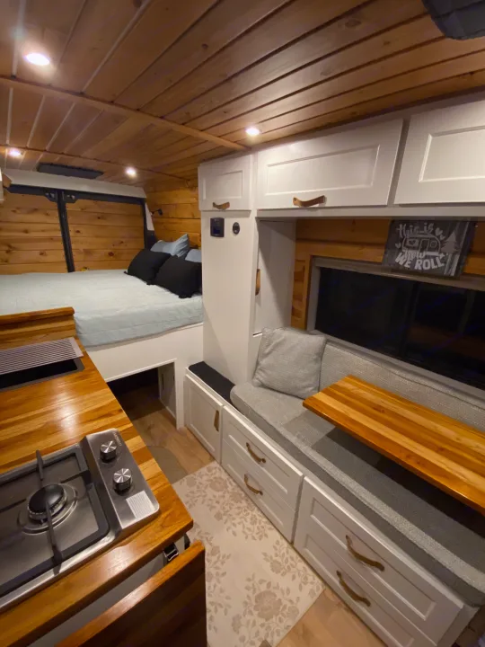 Inside a stylish RV rental: wood-paneled walls, a cozy bed, compact kitchen, and versatile seating.. RAM Promaster 2300 2023