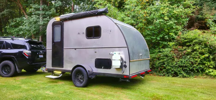 A silver teardrop camper, hitched to a black SUV and parked on green grass, is ideal for an rv rental.. Bend Teardrop Tall Boy 2023